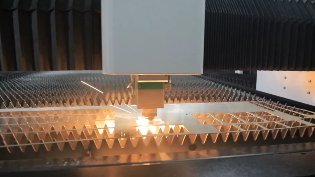 Gros plan sur une tête de découpe au laser à fibre concentrant le faisceau en un point de taille de l'ordre du micron sur une tôle d'acier inoxydable, avec un portique CNC en arrière-plan