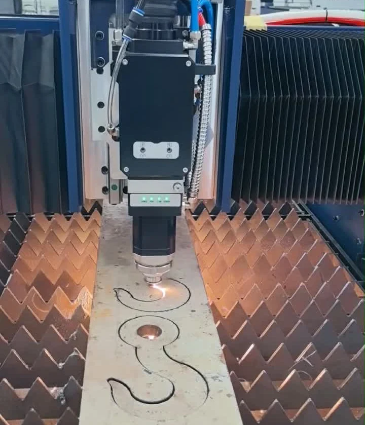 High-power fiber laser cutting machine processing thick carbon steel ship hull plates in heavy shipbuilding facility with bright sparks and protective enclosure