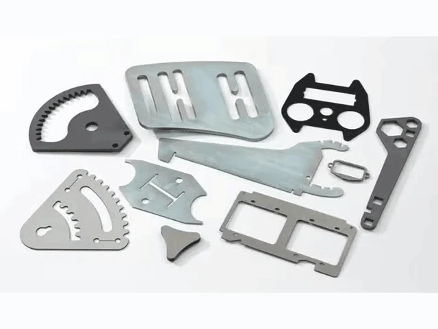 Array of precision laser-cut micro parts including nitinol stent segments, copper RF shield apertures, and titanium shims arranged on a measurement grid with digital caliper for scale reference