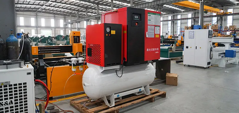 Screw air compressor system installed beside a fiber laser cutting machine in a workshop