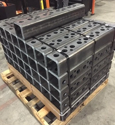 Stack of finished laser-cut tube and sheet parts next to remnant bin and production schedule board