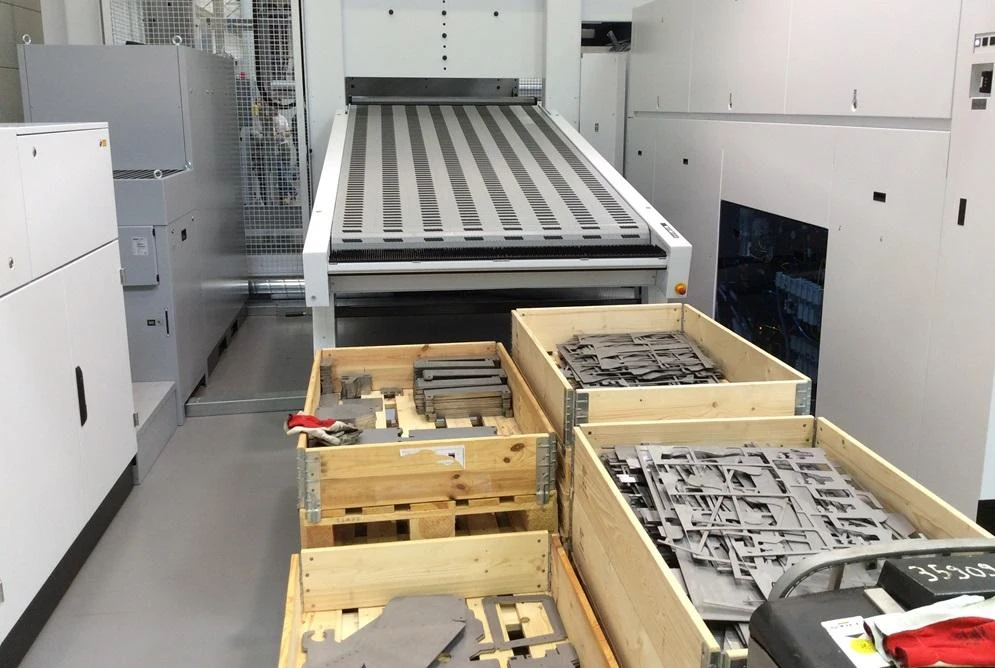 Stacked metal sheets on pallets beside a fiber laser cutting machine
