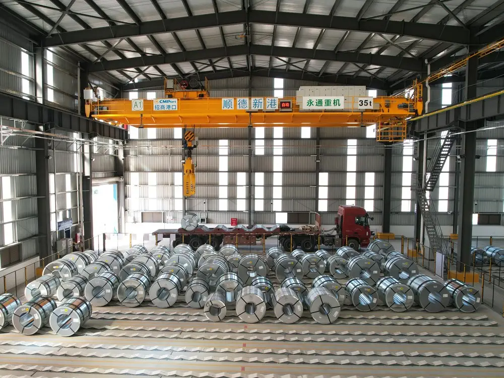 Heavy master steel coils stacked in an industrial warehouse with overhead crane for laser blanking operations