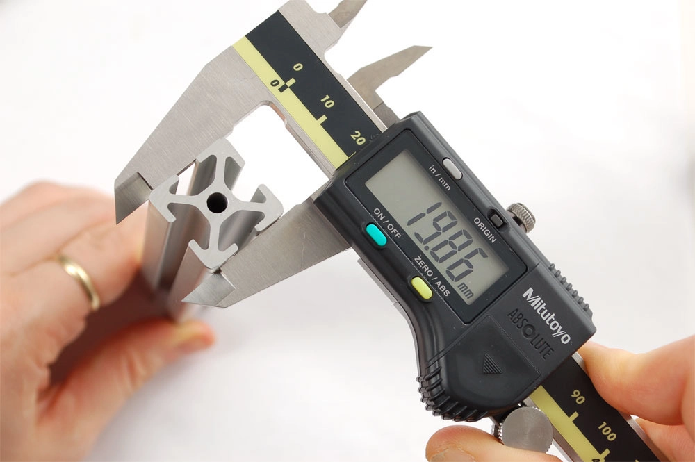 Quality control technician measuring laser cut part tolerance with digital caliper