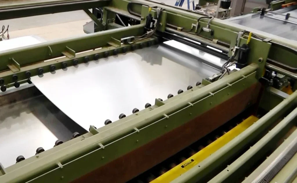 Flat sheet metal strip feeding through multi-roll precision leveler rollers on a coil-fed processing line