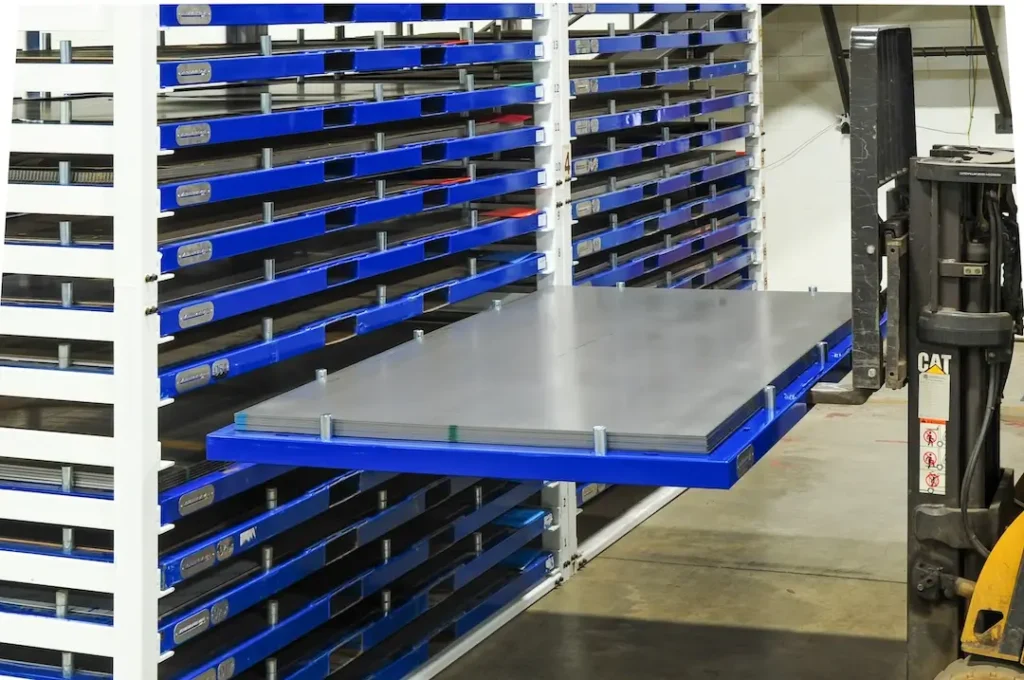 Stacked sheet metal on pallets and a forklift inside a fabrication shop