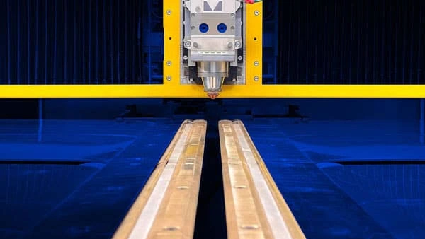 Steel strip passing through the continuous laser cutting zone of a blanking line with nested profiles cut directly from coil