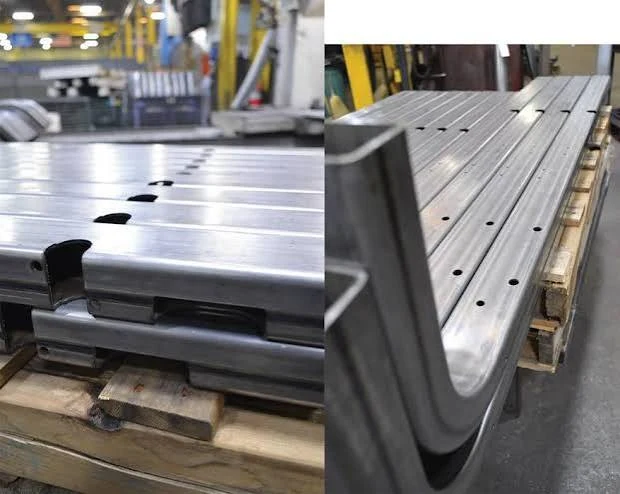 Finished laser cut sheet metal parts and slotted steel tubes staged on workshop pallet