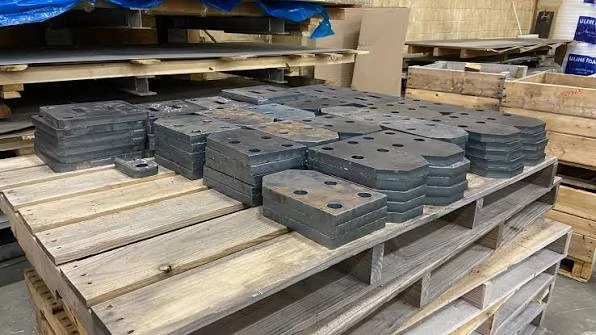 Heavy laser cut steel plate components stacked on pallets with batch tracking tags in fabrication facility